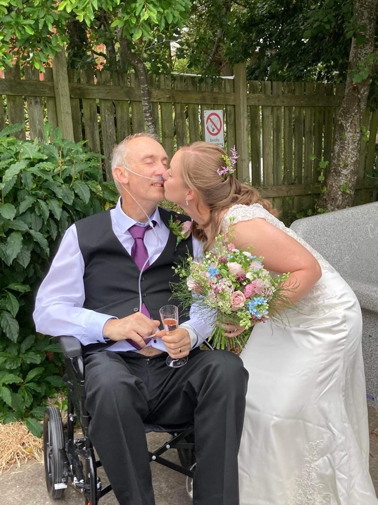 A bride kissing her terminally ill husband / groom in a wheelchair.