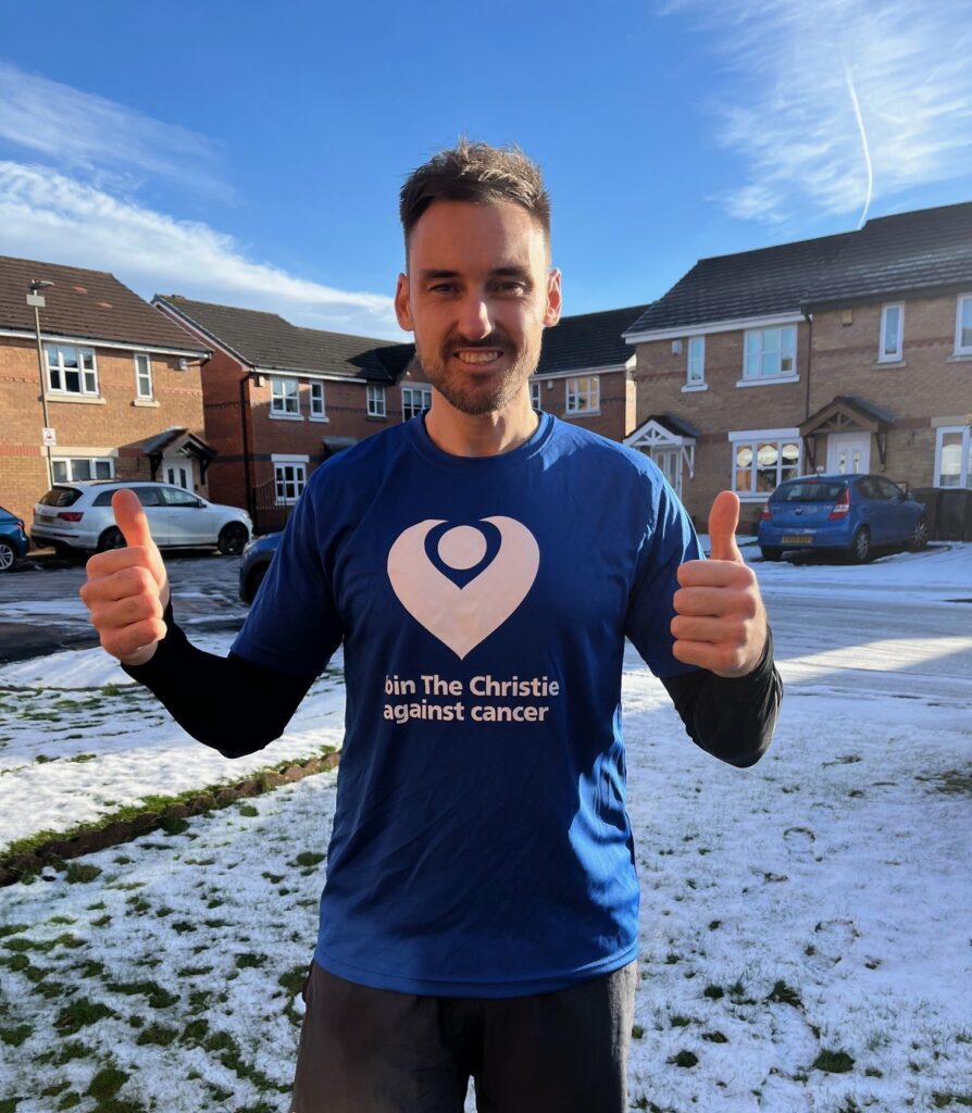 A man going for a run and giving a thumbs up in a charity t-shirt, against a snowy background.