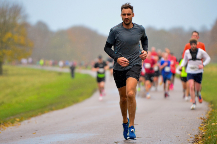 A determined-looking man in a grey top running down a path with other runners behind him.