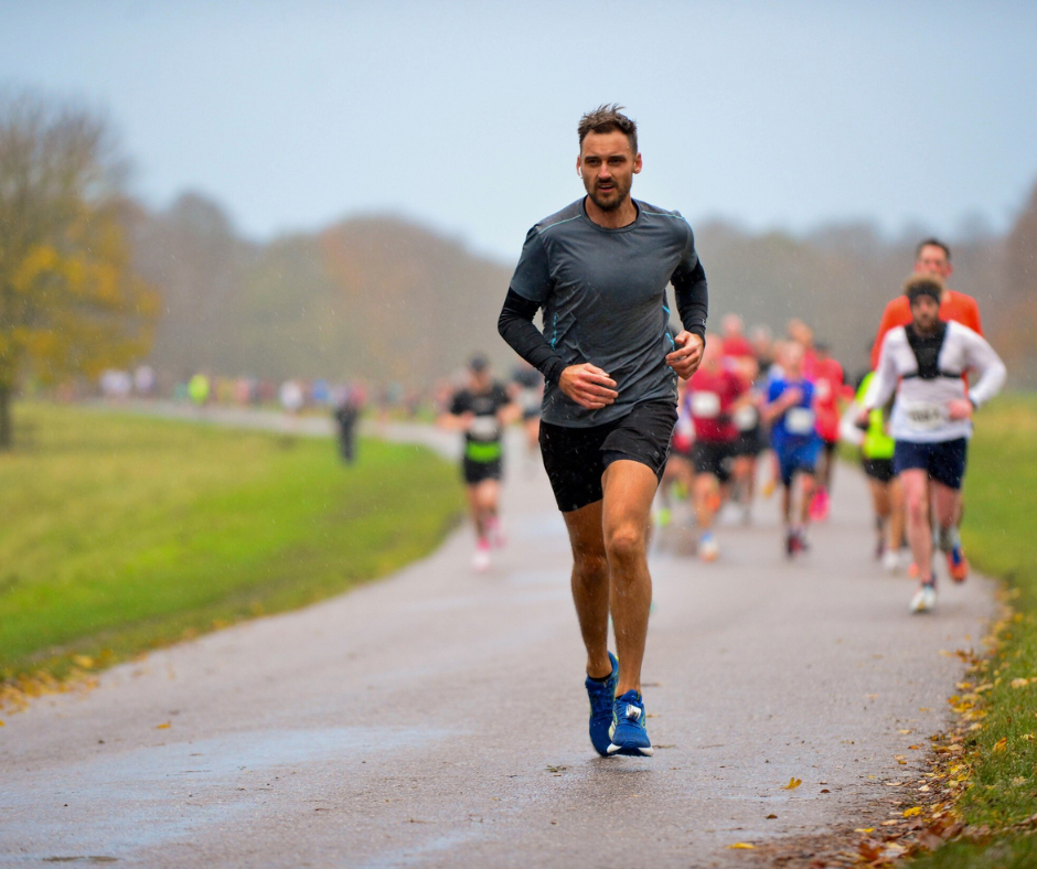 A determined-looking man in a grey top running down a path with other runners behind him.