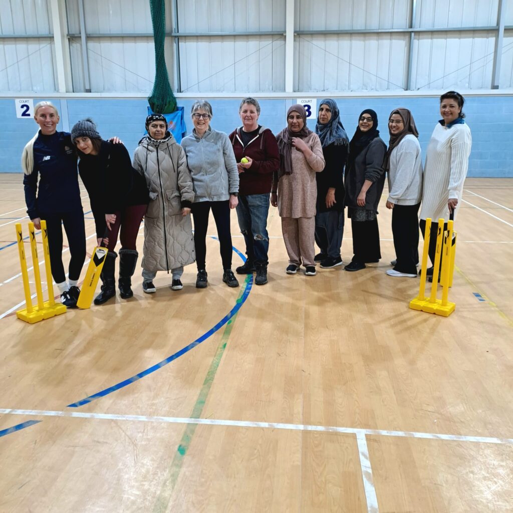 Group photo of women cricket players in sports hall.